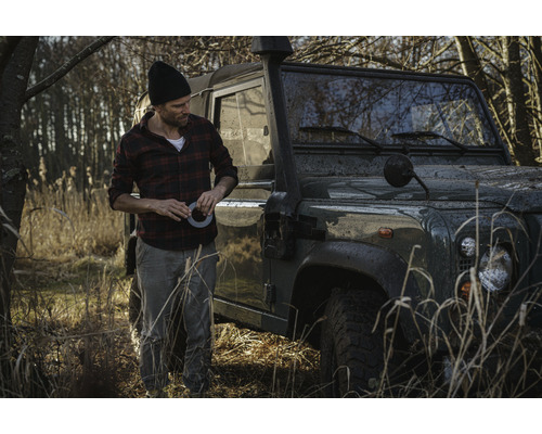 Mann mit Klebeband neben Geländewagen im Gelände