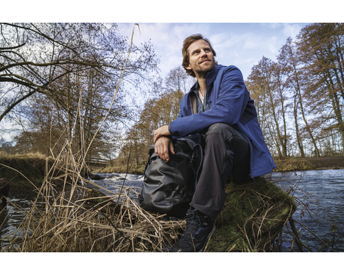 Mann mit Rucksack sitzt am Flussufer in der Natur