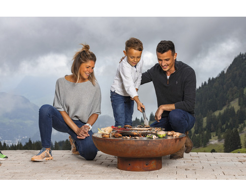 Familie grilliert auf einer Feuerstelle im Freien mit Bergkulisse