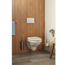 Wandhängendes WC mit Betätigungsplatte, Toilettenbürste und Toilettenpapierhalter in einem Badezimmer.