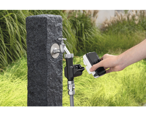 Scène de jardin avec robinet sur un socle en pierre et une personne connectant un dispositif d''arrosage