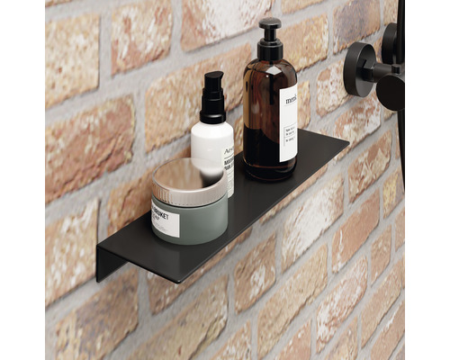 Étagère murale noire dans une salle de bain avec des produits de soins sur un fond de briques.