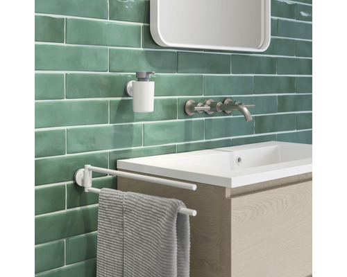 Lavabo de salle de bain avec robinet, distributeur de savon et porte-serviettes devant un mur vert.