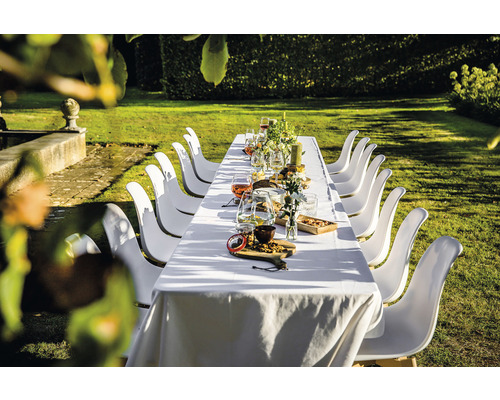 Longue table dressée dans le jardin avec des chaises blanches pour une fête