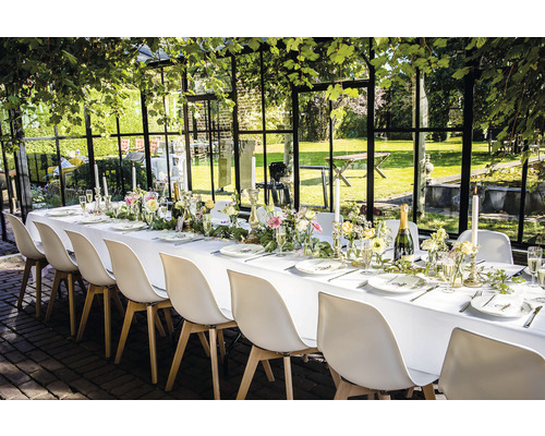 Table dressée pour une fête avec des chaises blanches dans une serre de jardin.