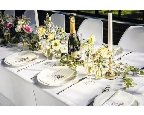 Table dressée avec assiettes, couverts, verres, fleurs, bougies et une bouteille de vin mousseux pour une célébration