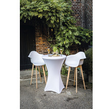 Table haute avec housse stretch et tabourets de bar devant un mur de briques avec végétation