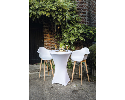 Table haute avec housse stretch et tabourets de bar devant un mur de briques avec végétation