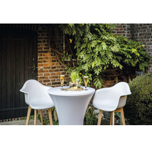 Scène extérieure avec une table haute, deux chaises, des boissons et des collations devant un mur de briques et des plantes.