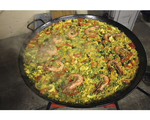 Paella mit Reis, Gemüse und Crevetten in einer grossen Pfanne.