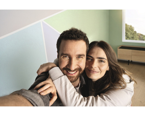 Glückliches Paar in einem frisch renovierten, hellen Raum mit farbigen Akzenten an der Wand