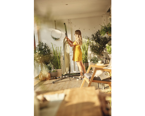 Une femme prépare un hamac avec support sur un balcon, entouré de plantes.