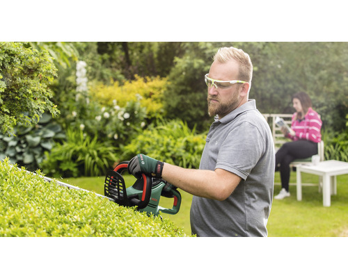 Mann schneidet Hecke mit Heckenschere im Garten