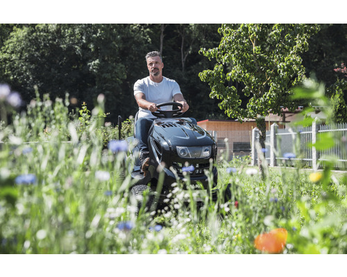 Un homme conduit un tracteur de jardin dans un jardin avec des fleurs.