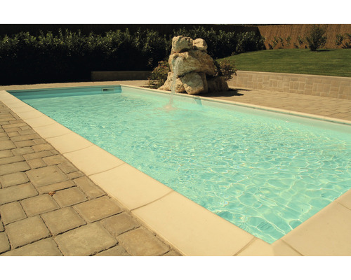 Piscine avec bordure en pierre et terrasse carrelée dans un jardin.