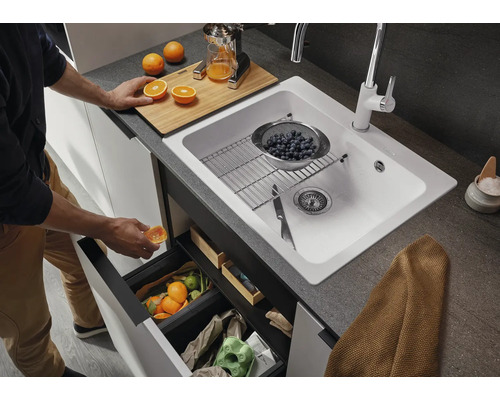 Scène de cuisine avec évier, robinet, poubelle et aliments sur un plan de travail.