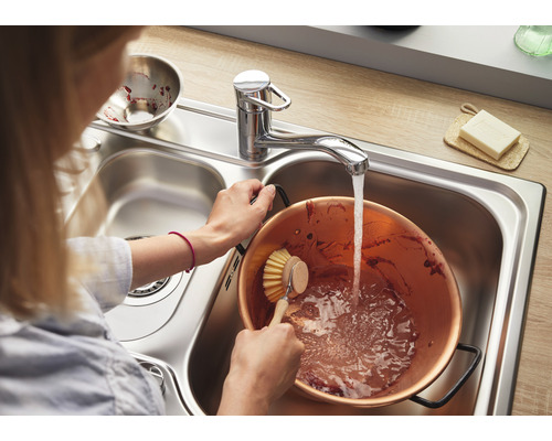 Femme lavant une bassine à confiture en cuivre dans un évier en acier inoxydable avec robinet.