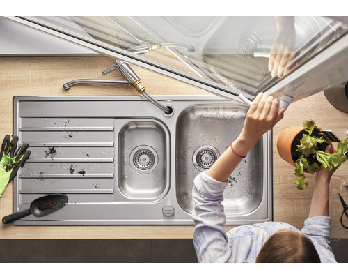 Edelstahlspüle mit Armatur und Person, die eine Pflanze hält