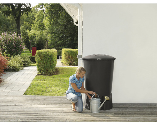 Frau befüllt Giesskanne an Regentonne im Garten