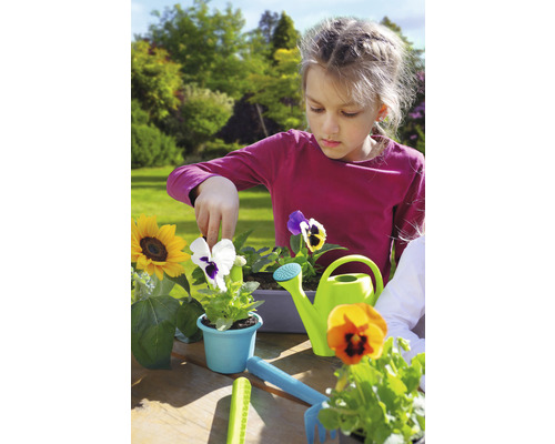 Fille plante des fleurs dans le jardin avec un arrosoir et des outils de jardinage