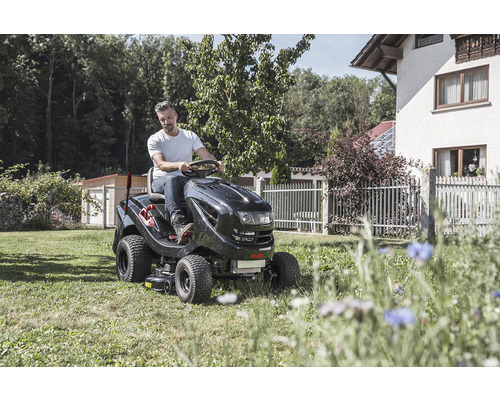 Un homme conduit un tracteur de jardin sur une pelouse devant une maison