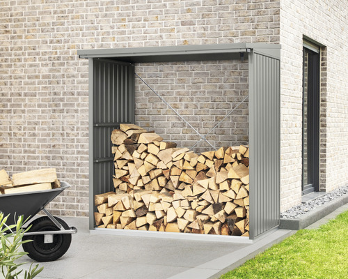 Abri à bois en métal avec des bûches devant un mur de briques