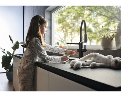 Fille remplissant un verre d''eau à un robinet de cuisine noir