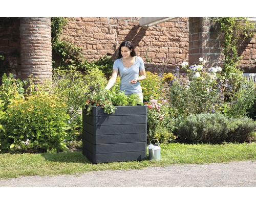 Femme jardine dans un bac à fleurs noir dans le jardin