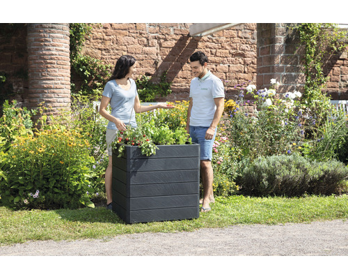 Un couple regarde un bac à fleurs rectangulaire planté dans le jardin.