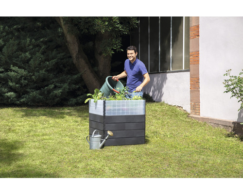 Jardinière en imitation bois avec un homme qui ajoute des plantes, et un arrosoir dans le jardin