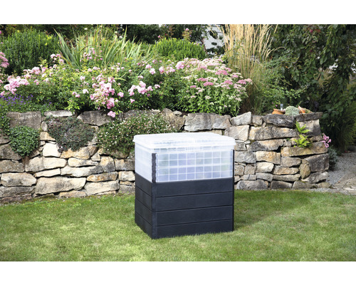 Composteur en plastique dans le jardin devant un mur de pierre et des parterres de fleurs