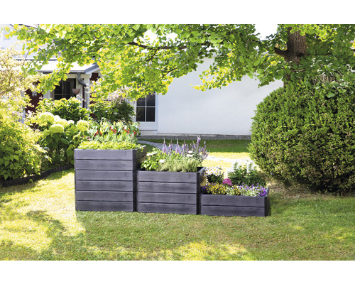 Trois jardinières en bois de différentes hauteurs dans le jardin, plantées de fleurs