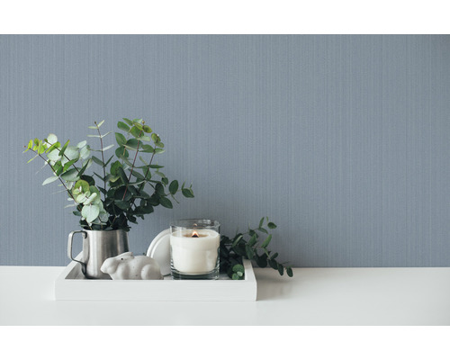 Scène décorative avec papier peint, bougie et eucalyptus sur un plateau.