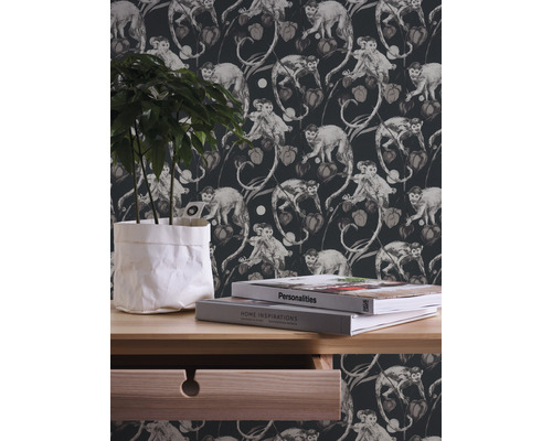 Dekorative Tapete mit Affen- und Pflanzenmotiven im Hintergrund, dazu eine Kommode mit Pflanze und Büchern.