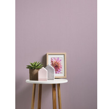 Nahaufnahme einer Wand mit Texturtapete, dekoriert mit einer Zimmerpflanze, einem Bilderrahmen und zwei Zierhäusern auf einem kleinen Tisch.