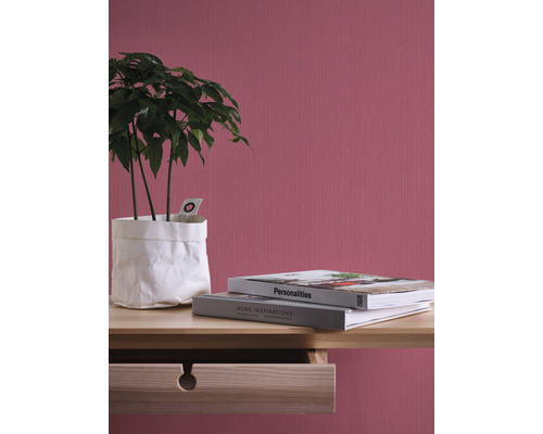 Dekorative Zimmerpflanze in weissem Papierbehälter auf einem Holztisch mit zwei Büchern vor einer strukturierten Wand