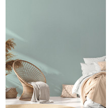 Helles Schlafzimmer mit Korbsessel, Bett und Trockenblumen