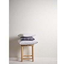 Scène avec tabouret et coussins empilés devant un mur à motif à pois.