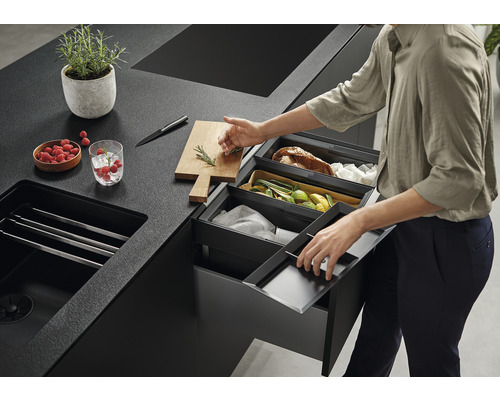 Scène de cuisine avec poubelles de tri sélectif, évier, planche à découper, couteau, bol de framboises et plante en pot