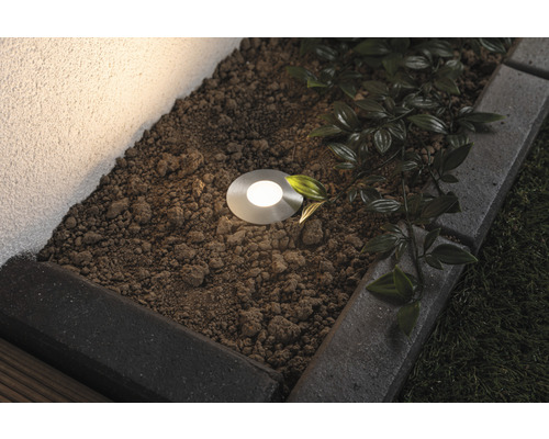 Bodeneinbaustrahler in einem Gartenbeet mit Pflastersteinen und Bepflanzung.