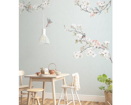 Esszimmer mit hellem Holztisch, Stühlen, Hocker, Geschirr, Zimmerpflanze und einer Wandtapete mit Vogel- und Blütenmotiven.