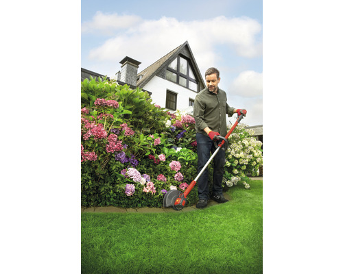 Un homme coupe l''herbe avec un coupe-bordures dans le jardin devant une maison.