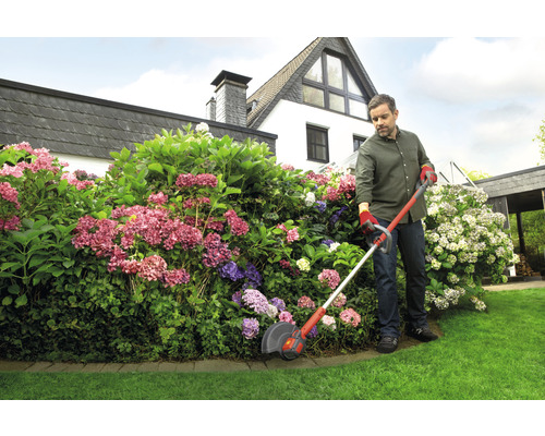 Un homme utilise un coupe-bordure pour couper l''herbe le long d''un parterre de fleurs.