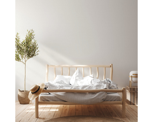 Helles Schlafzimmer mit Holzbett, Bettwäsche, Pflanze und Strohhut.