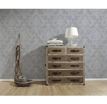 Szene mit gemusterter Tapete, Holzkommode mit Schubladen, Tischlampe und dekorativen Elementen