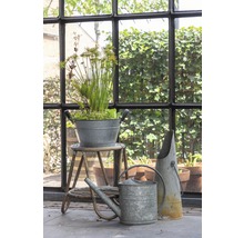 Scène de jardin décorative avec arrosoir en zinc, jardinière et transplantoir devant une fenêtre