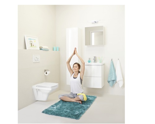 Helles Badezimmer mit Toilette, Waschbecken, Spiegel und einer Frau beim Yoga auf einem Teppich