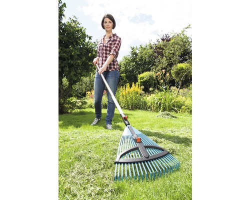 Eine Frau benutzt einen Laubbesen im Garten, um Gras zu rechen.