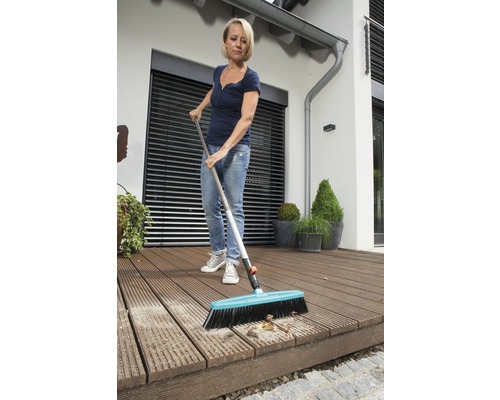 Frau reinigt eine Holzterrasse mit einem Strassenbesen.
