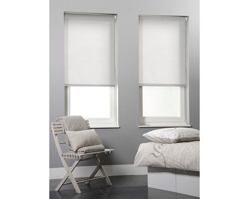 Zwei weisse Rollos an Fenstern in einem Schlafzimmer mit einem Stuhl und einem Bett